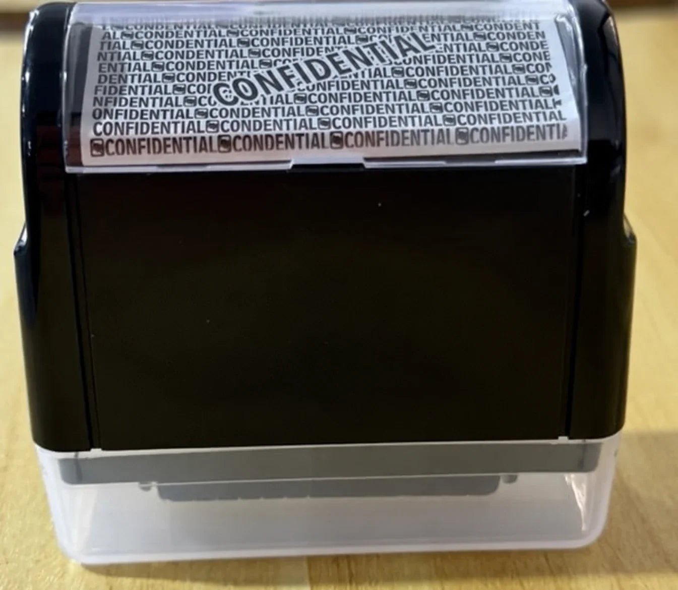 A black privacy roller with a clear cap photographed on a tan surface